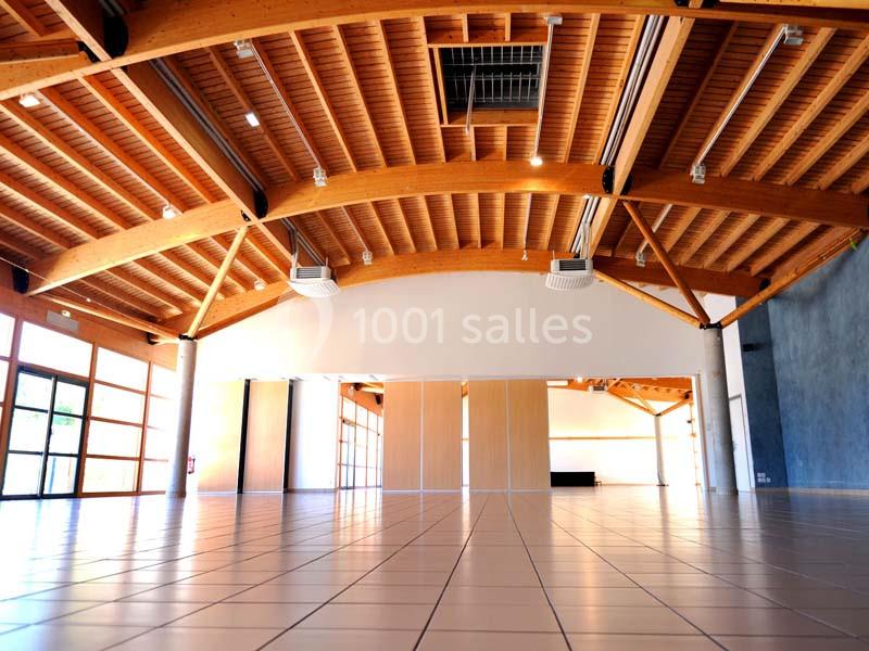 Grande salle lumineuse avec charpente en bois apparente, sol carrelé et larges baies vitrées.
