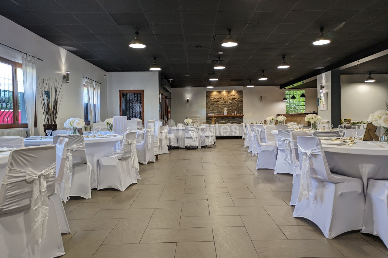 Salle de réception élégamment décorée avec des tables rondes, nappes blanches et chaises couvertes de housses.
