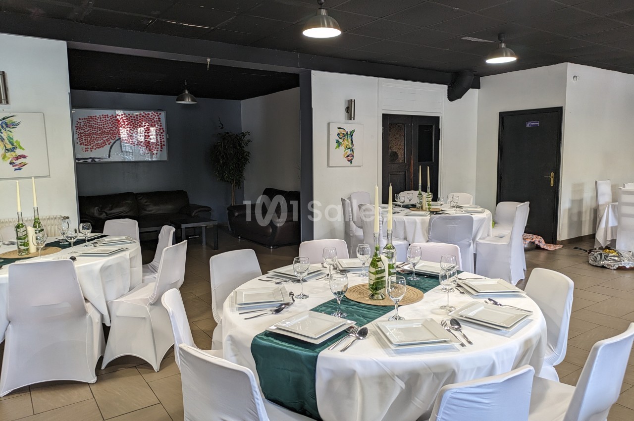 Salle de réception avec tables rondes dressées, nappes blanches, chemins de table verts et chaises houssées.