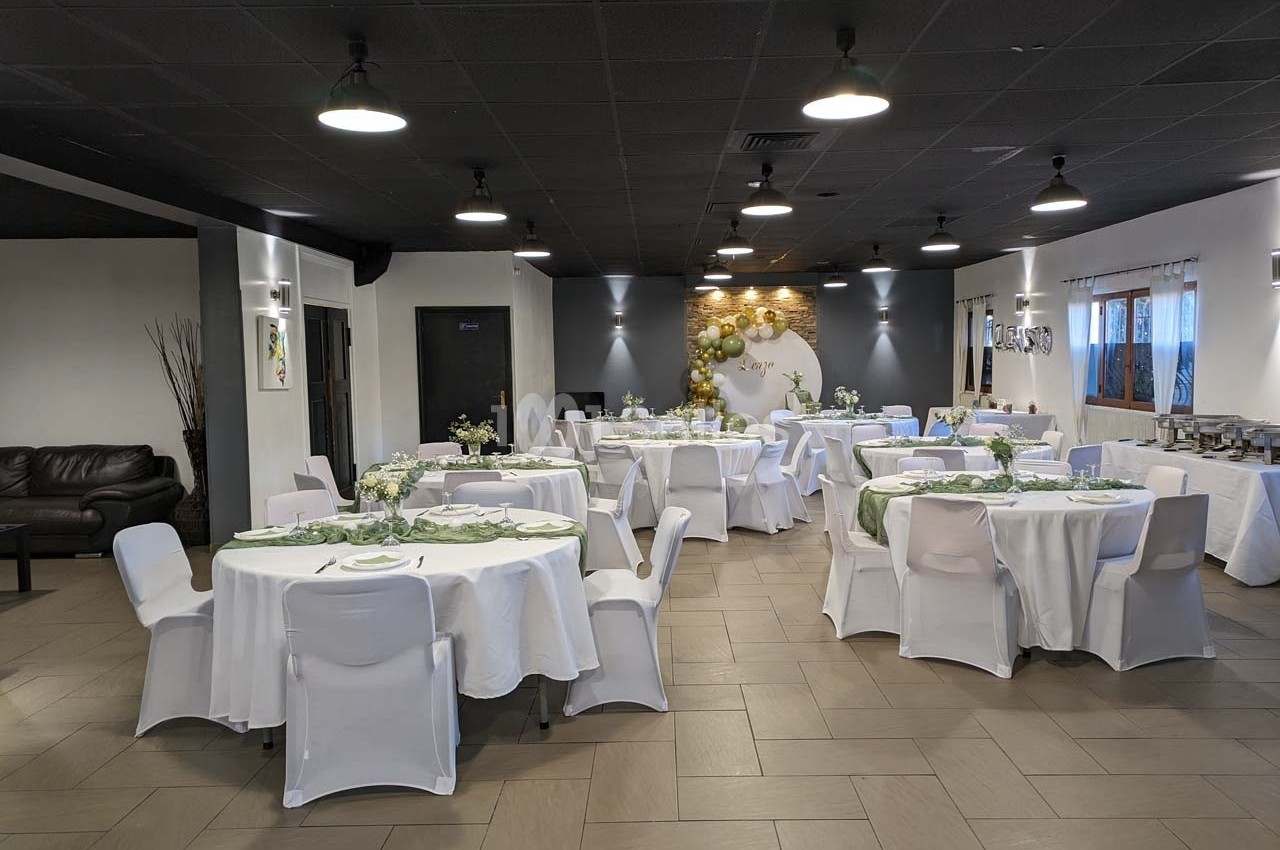 Salle de réception décorée avec des tables rondes dressées, nappes blanches et ballons dorés en arrière-plan.