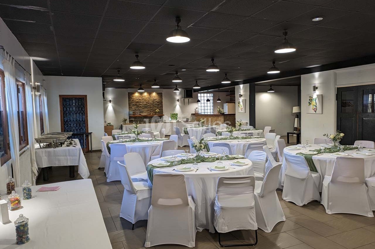 Salle de réception décorée avec des tables rondes dressées, nappes blanches et chaises houssées, éclairage tamisé.