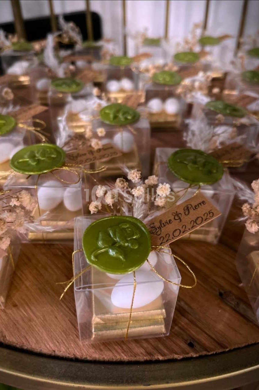 Petites boîtes transparentes contenant des dragées blanches, décorées de cachets de cire verte et de fleurs séchées.