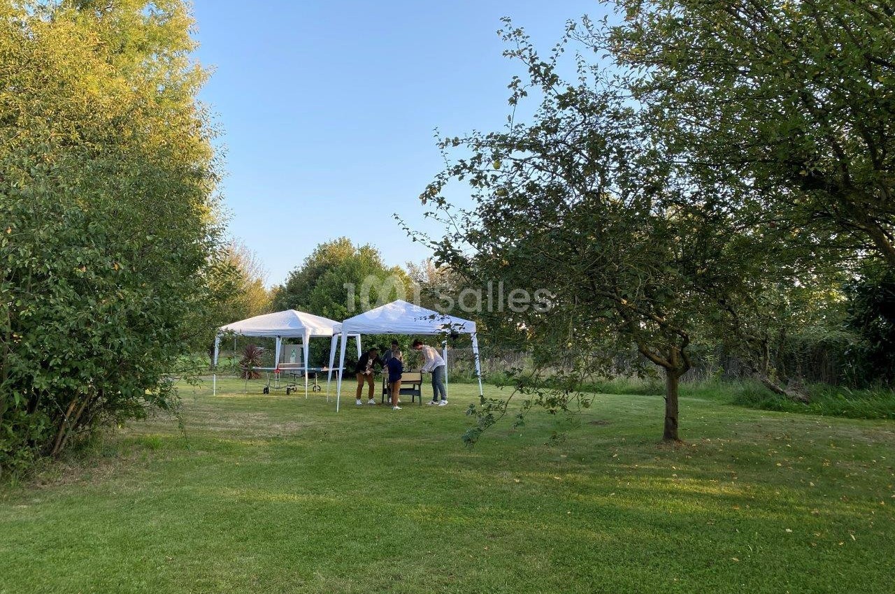 Deux tentes blanches installées dans un jardin verdoyant, avec quelques personnes debout à proximité.
