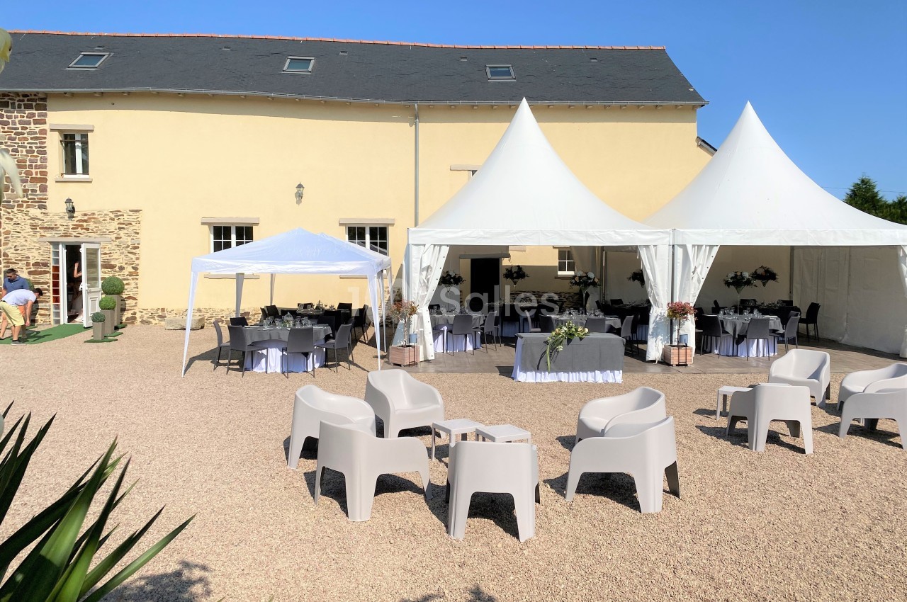Espace extérieur avec barnums et chaises installés devant un bâtiment en pierre pour un événement en plein air.