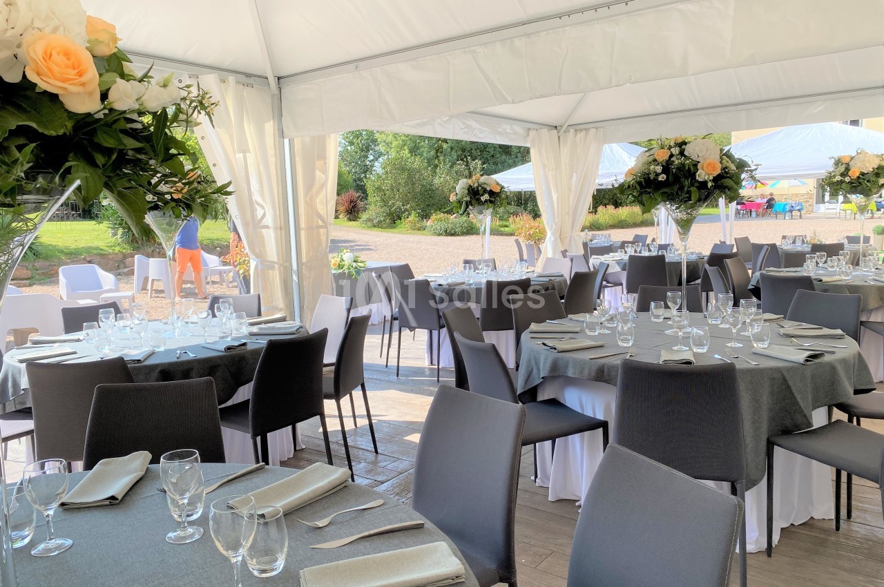 Salle de réception décorée avec des tables rondes, nappes grises, chaises noires et arrangements floraux.