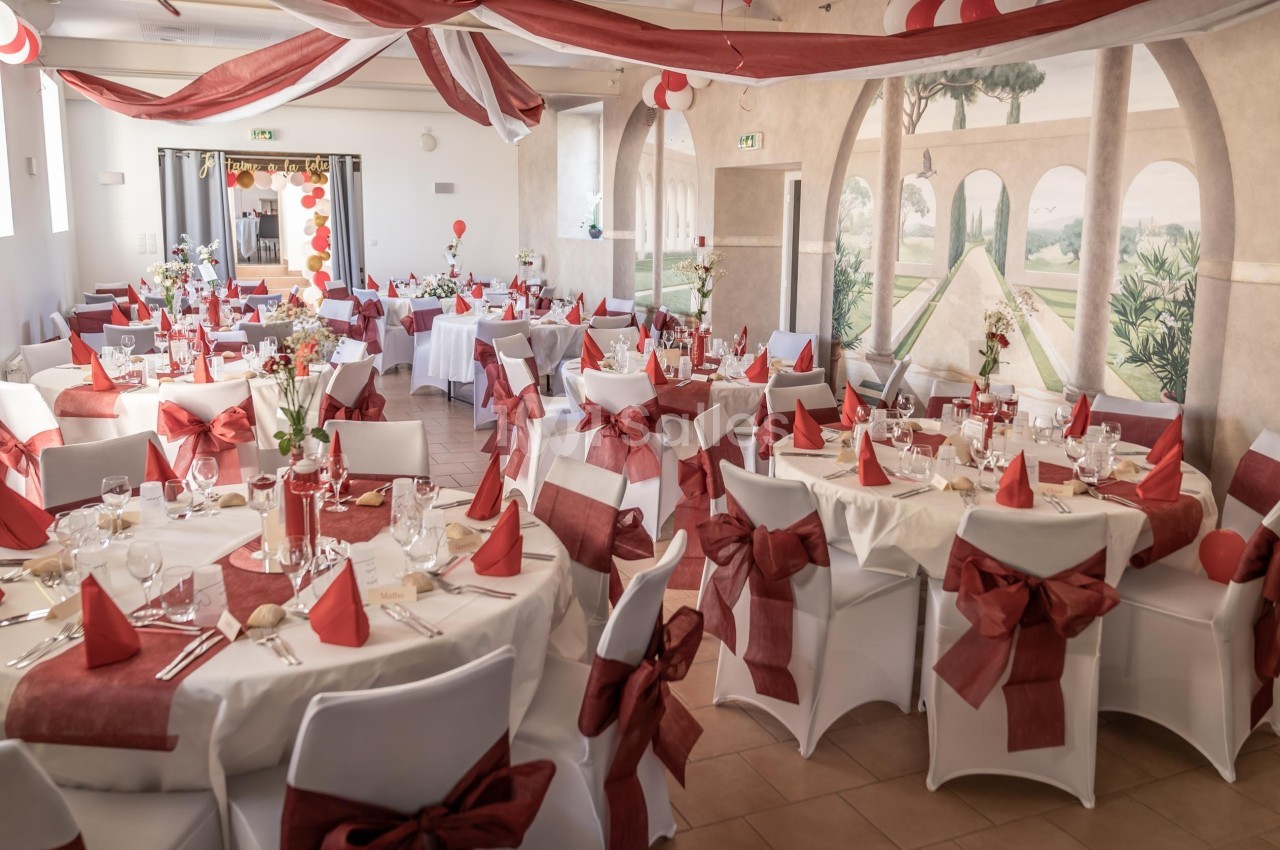 Salle de réception décorée avec des nappes blanches, des nœuds rouges sur les chaises et des tables dressées pour un…