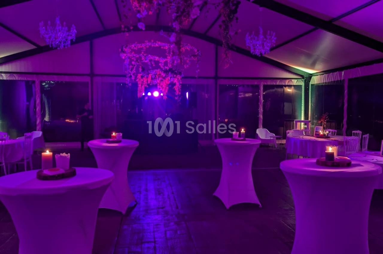 Salle de réception éclairée par des lumières violettes, avec tables hautes décorées de bougies et un espace central dégagé.