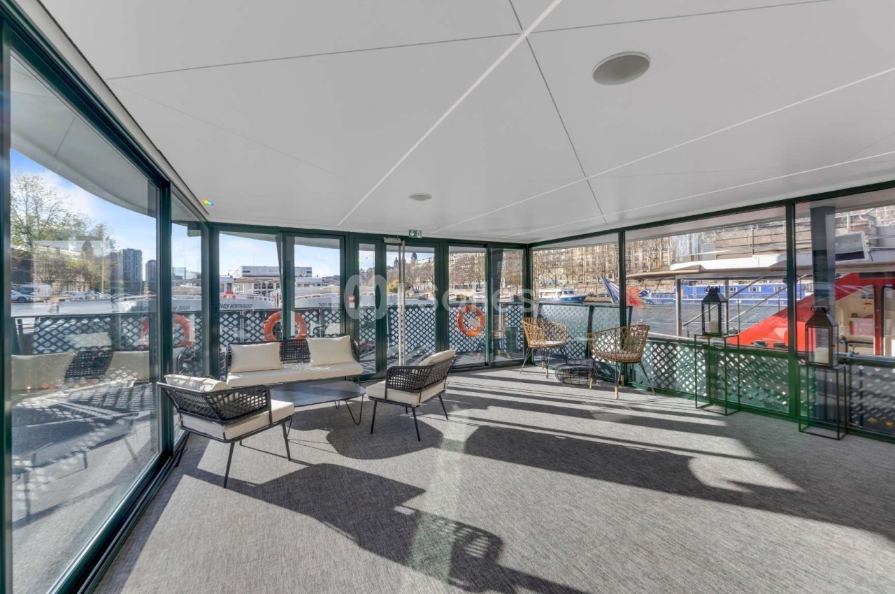 Espace intérieur lumineux avec baies vitrées donnant sur un quai, aménagé avec des fauteuils et une table basse.