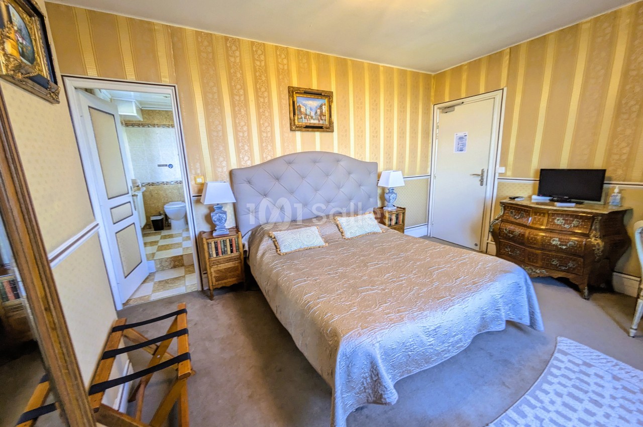 Chambre avec lit double, mobilier classique, murs à rayures jaunes et accès à une salle de bain adjacente.