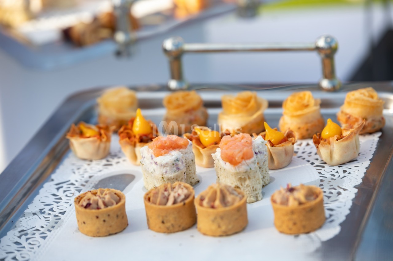 Plateau de canapés variés comprenant des bouchées au saumon, fromage et autres garnitures sur napperon blanc.