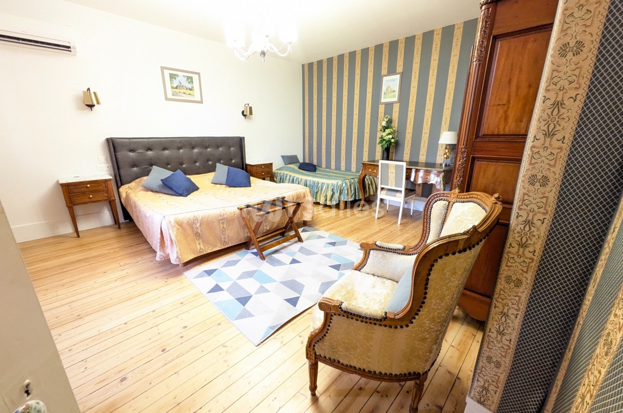 Chambre spacieuse avec lit double, lit simple, fauteuil, armoire en bois, parquet et décoration classique.
