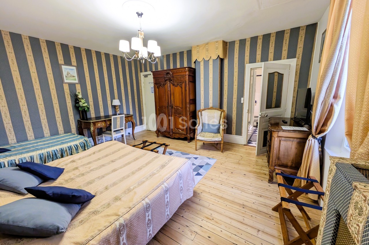Chambre spacieuse avec lit double, lit simple, armoire en bois, bureau, fauteuil et décoration classique.