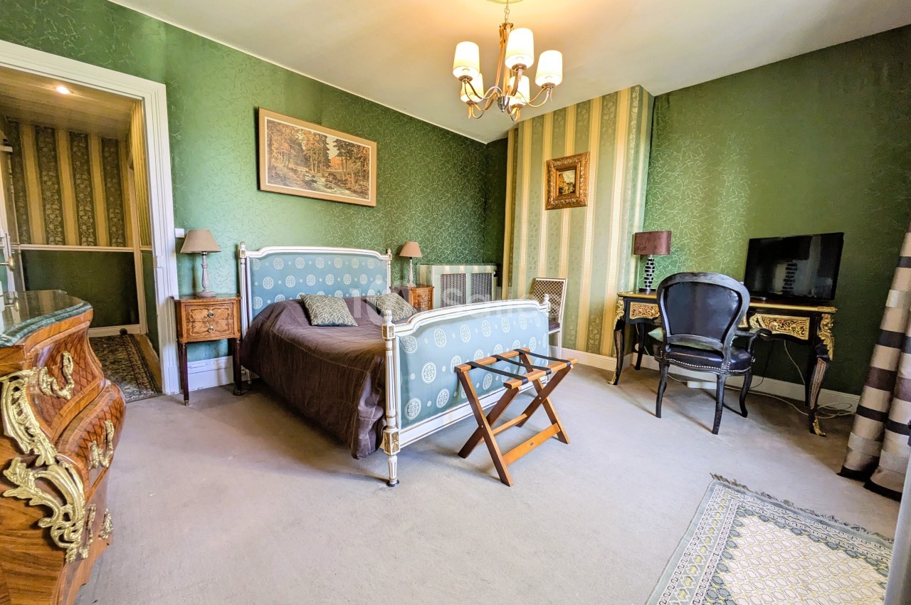 Chambre décorée de style classique avec lit double, mobilier ancien, murs verts et éclairage par un lustre.