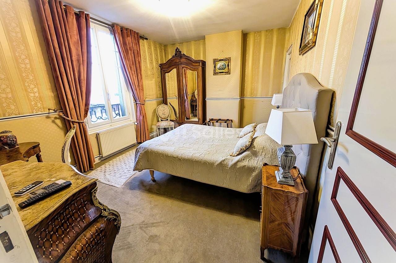Chambre avec lit double, armoire ancienne, commode sculptée, rideaux épais et lumière naturelle provenant d'une fenêtre.