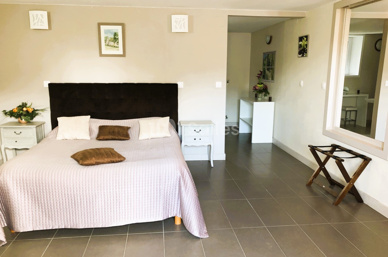 Chambre lumineuse avec lit double, tables de chevet, décoration murale et sol en carrelage gris.