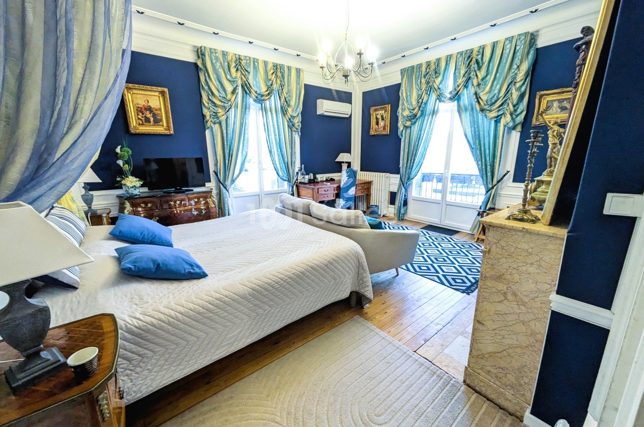 Chambre élégante avec murs bleus, lit double, rideaux luxueux, cheminée en marbre et meubles anciens.