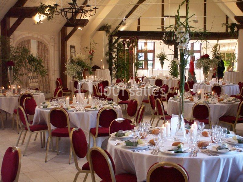 Salle de réception décorée avec des tables rondes dressées, chaises rouges et éclairage chaleureux.