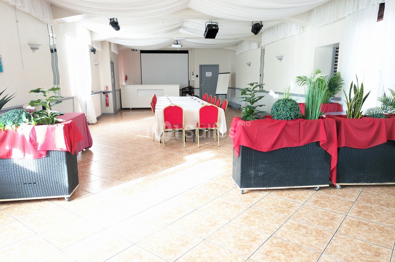 Salle lumineuse avec tables, chaises rouges et plantes décoratives, sous un plafond drapé de tissu blanc.