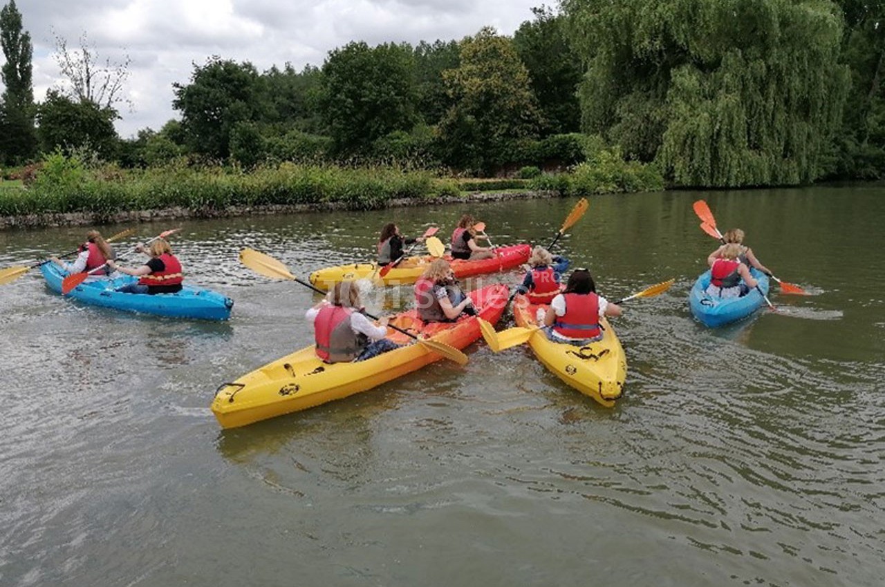 Des personnes pagayant en kayak sur une rivière entourée de végétation sous un ciel nuageux.