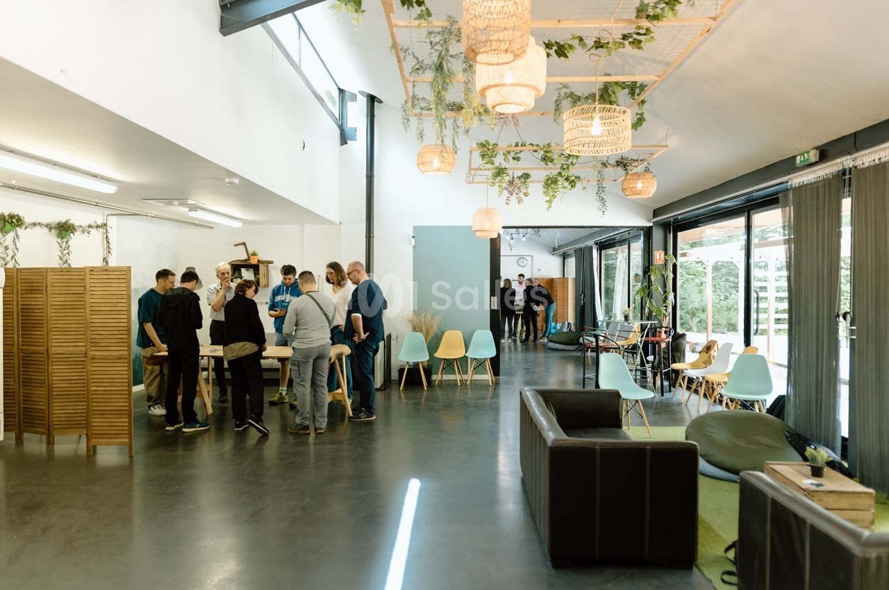 Un groupe de personnes échange dans un espace de coworking lumineux avec mobilier moderne et plantes suspendues.