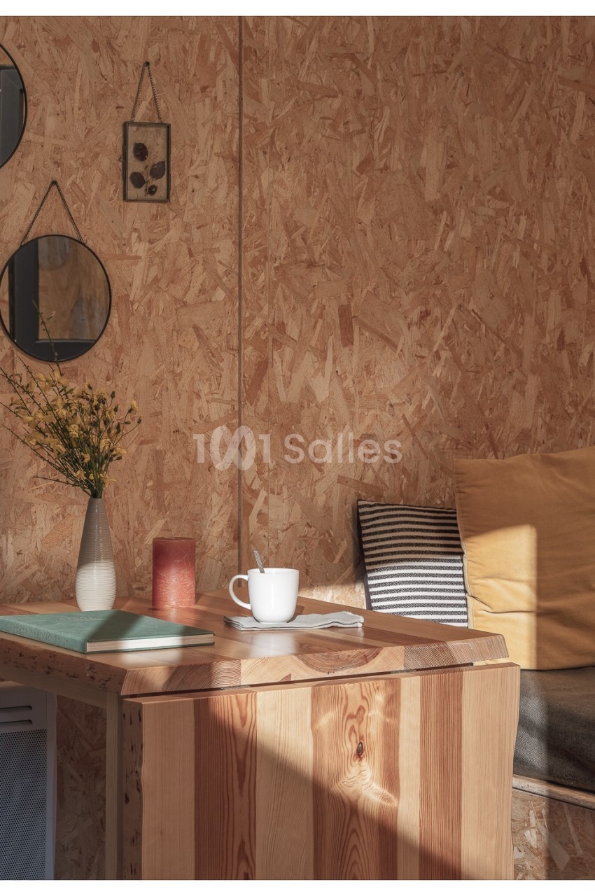 Espace intérieur chaleureux avec table en bois, vase de fleurs, tasse blanche et coussins sur un banc près d'un mur en OSB.