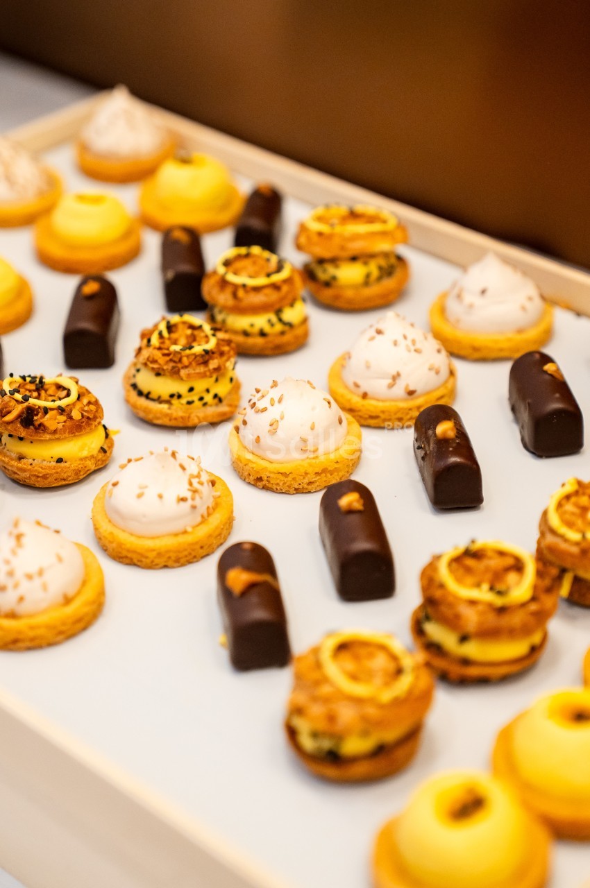 Plateau de pâtisseries variées comprenant éclairs au chocolat, tartelettes et choux garnis, disposés sur une surface blanche.