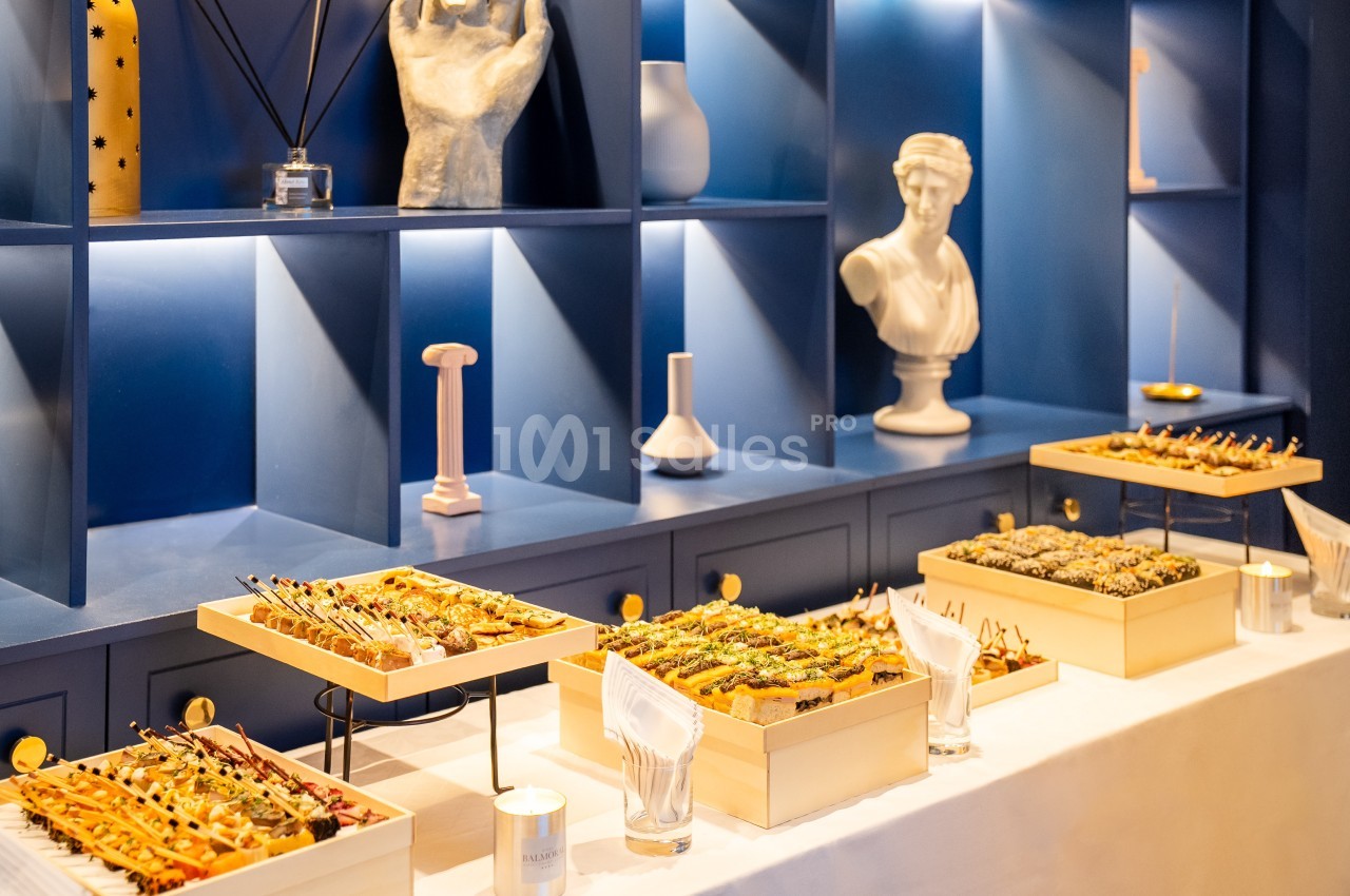 Plateau de brochettes variées disposé sur une table devant une étagère bleue décorée de statues et d'objets.