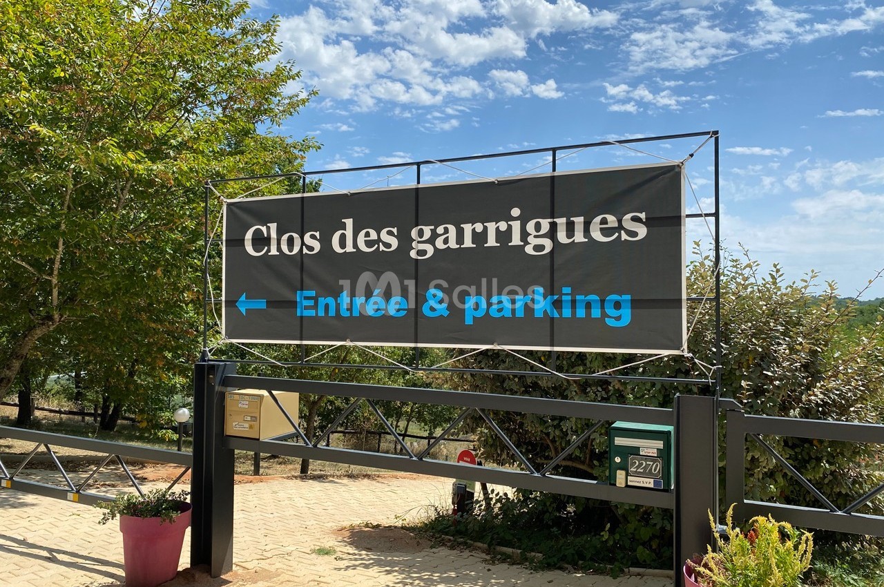 Panneau indiquant ’Clos des garrigues’ avec flèche vers l'entrée et le parking, situé devant une grille métallique.