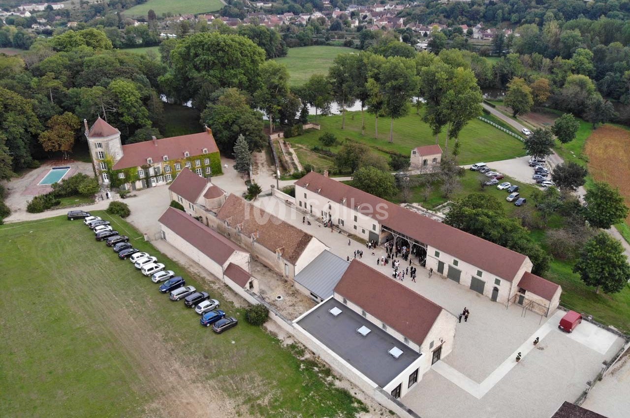 Vue aérienne d'un domaine rural avec bâtiments en pierre, cour centrale, piscine et voitures stationnées.
