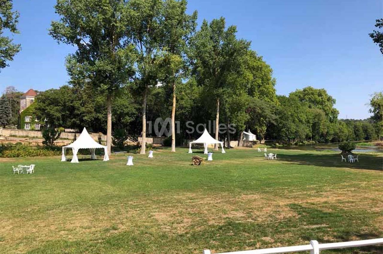Pelouse verdoyante avec des arbres, des tentes blanches et quelques tables et chaises disposées en extérieur.