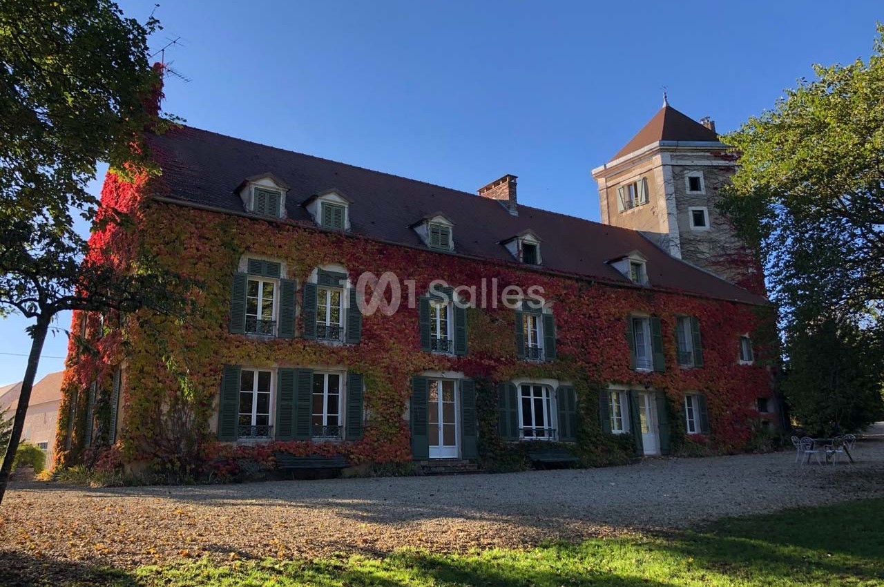Façade d'une grande maison en pierre recouverte de vigne rouge, avec une tour attenante, sous un ciel dégagé.