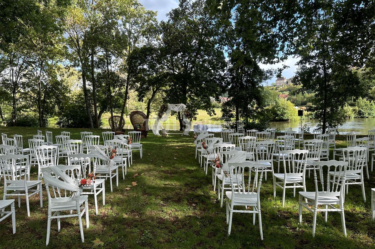 Chaises blanches disposées en rangées sur une pelouse, formant une allée centrale menant à une arche décorée pour une…