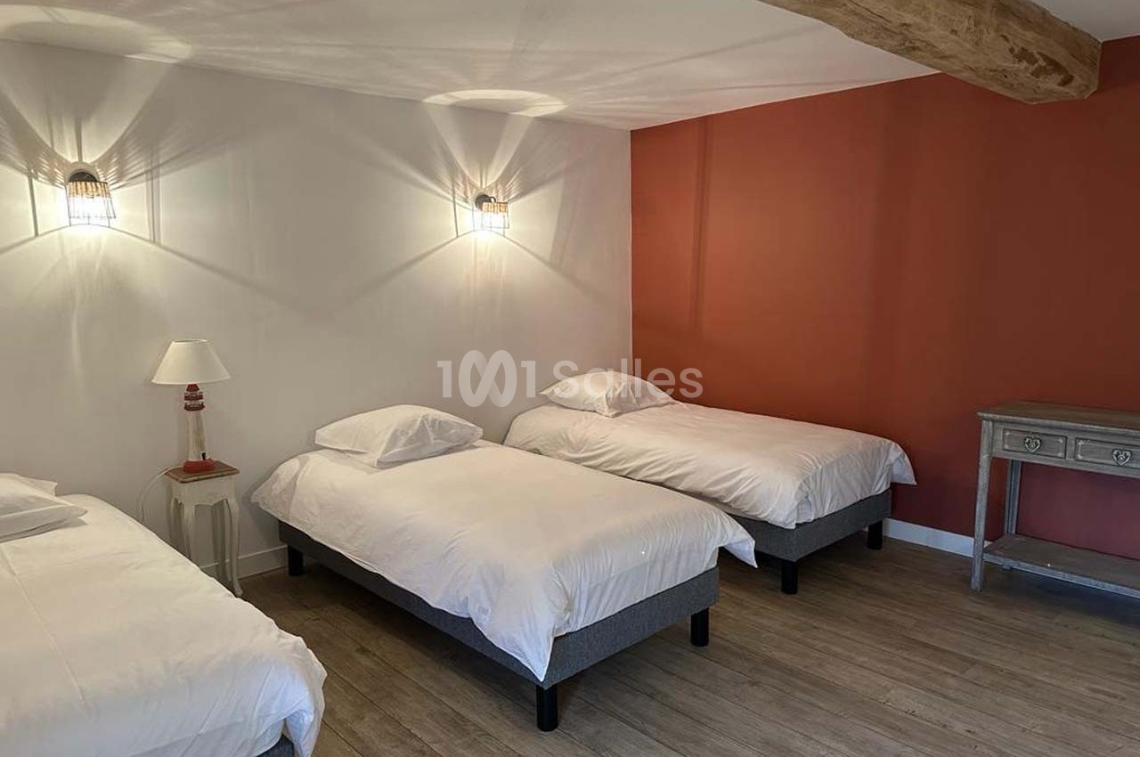 Trois lits simples avec draps blancs dans une chambre à la décoration sobre, mur orange et poutre apparente.