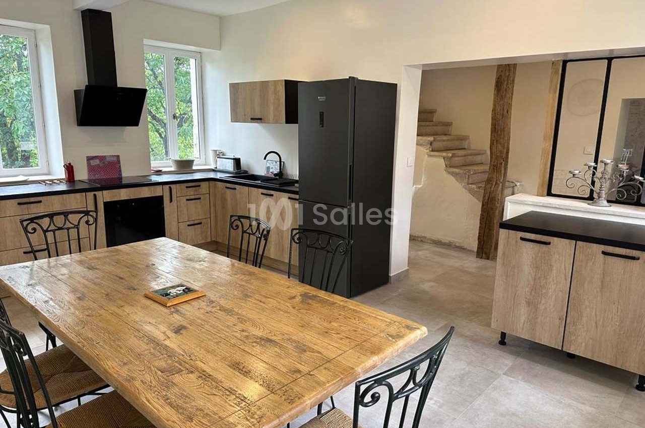Cuisine moderne avec table en bois, chaises en métal, meubles en bois clair, réfrigérateur noir et fenêtre donnant sur des…