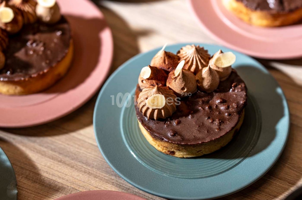 Tartelette au chocolat garnie de crème et décorée d'amandes effilées, servie sur une assiette bleue.