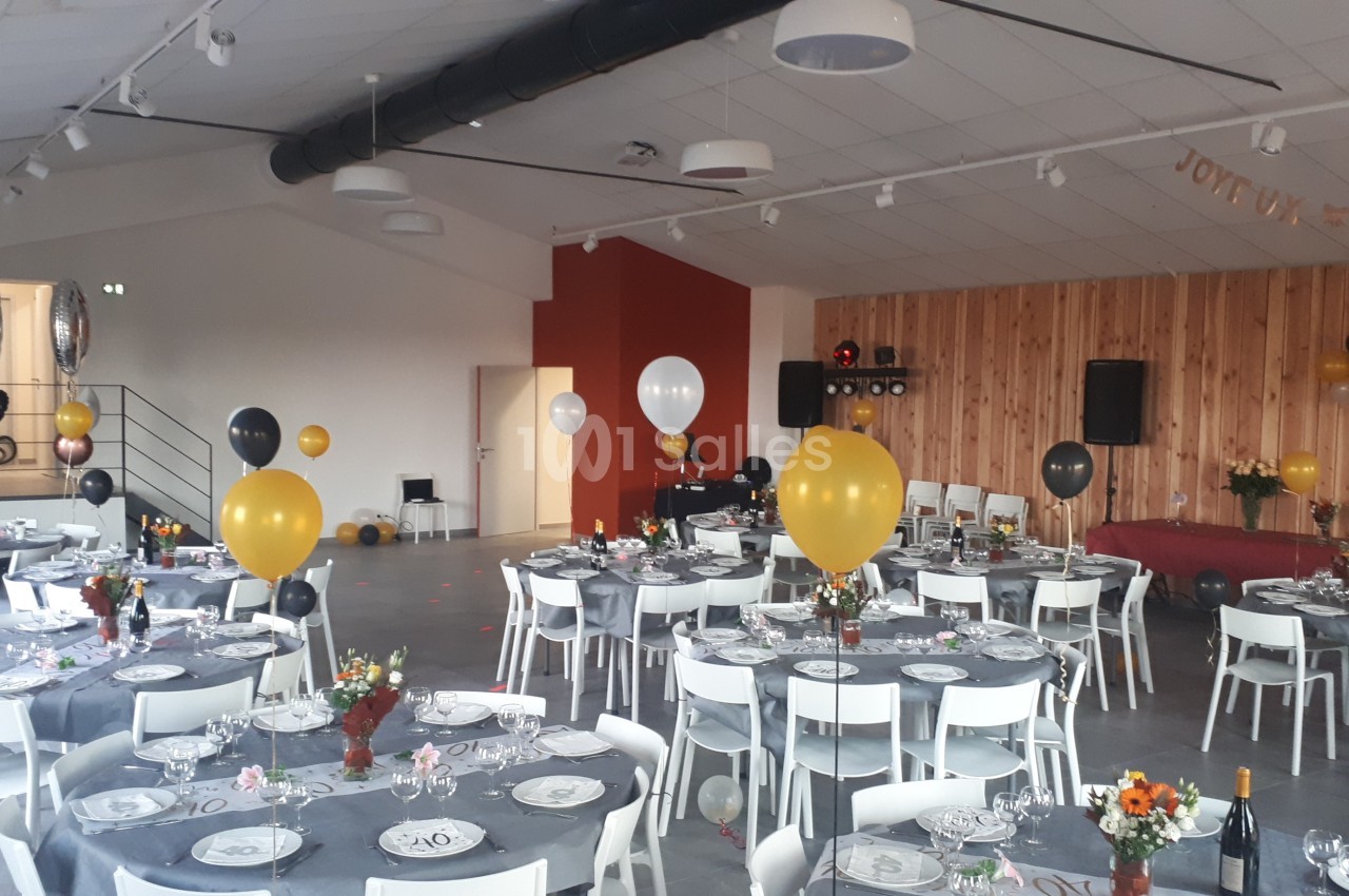 Salle décorée pour un événement avec des tables dressées, des ballons colorés et une ambiance festive.