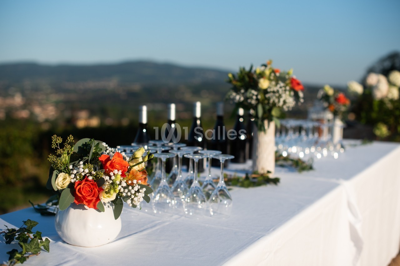 Table dressée en extérieur avec des bouquets de fleurs, des verres à vin et des bouteilles alignées.