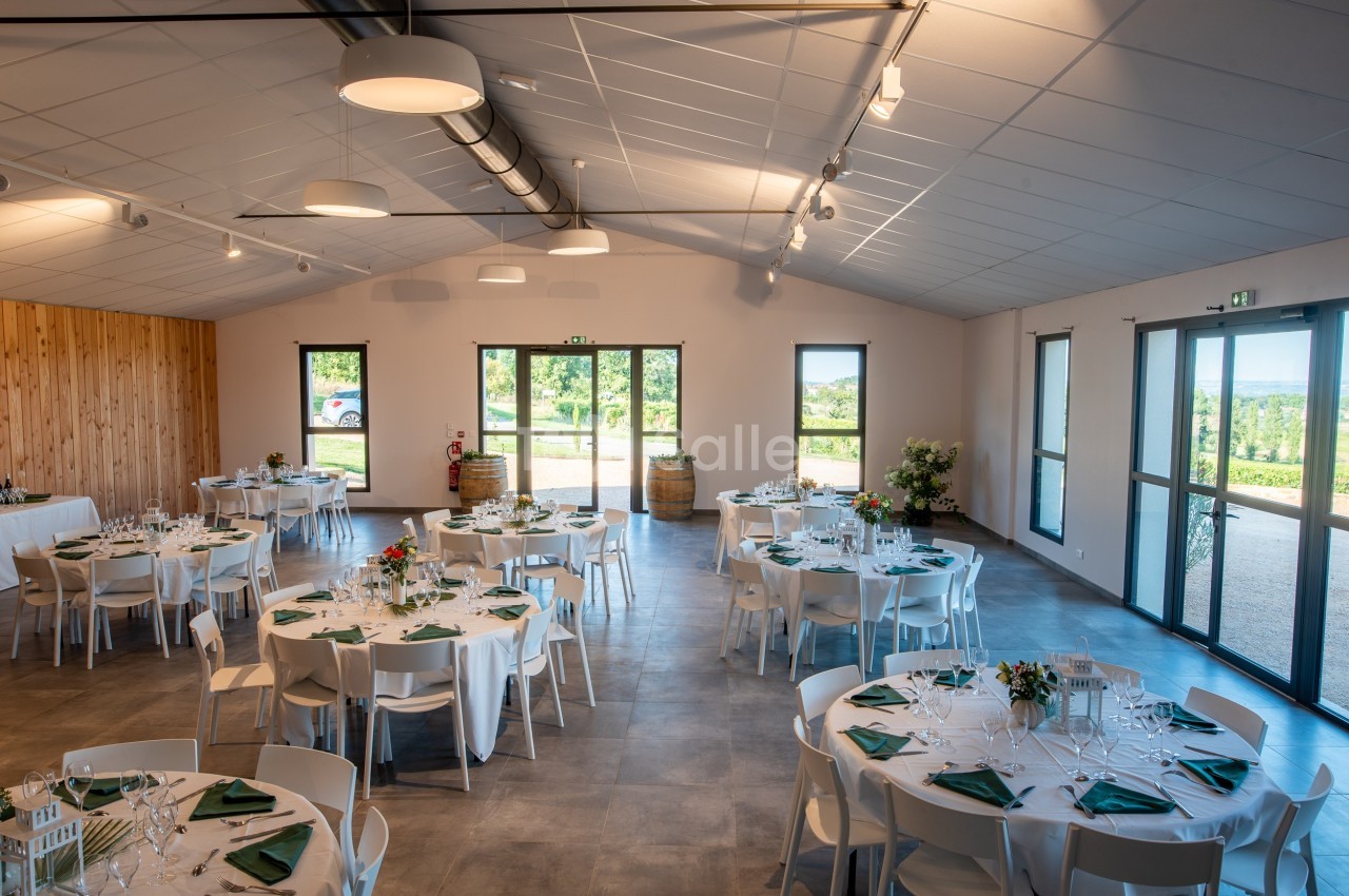 Salle de réception lumineuse avec tables rondes dressées, nappes blanches et serviettes vertes, vue sur l'extérieur…