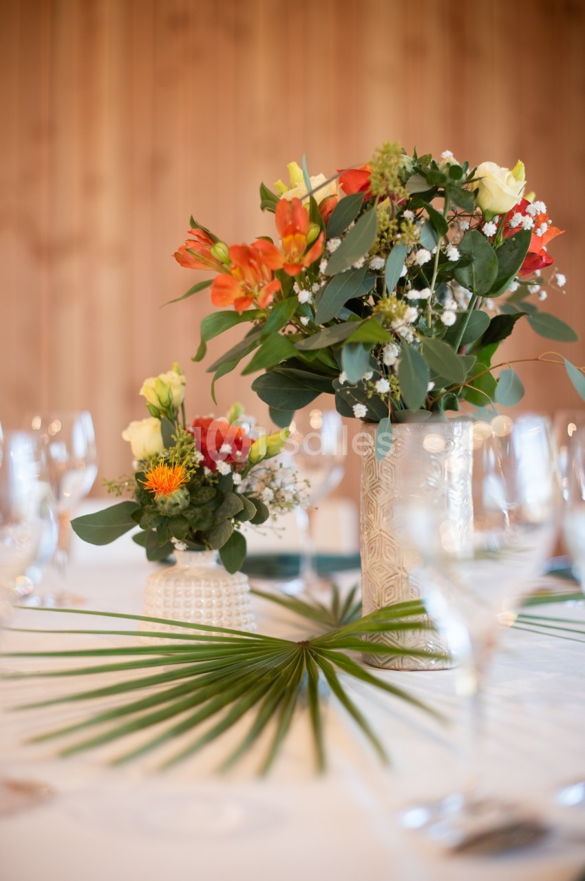 Deux vases décoratifs avec des fleurs colorées sur une table dressée, ornée d'une feuille de palmier.