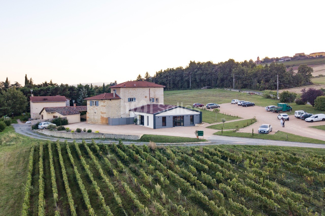Vue aérienne d'un domaine viticole avec bâtiments en pierre, vignes au premier plan et voitures stationnées.