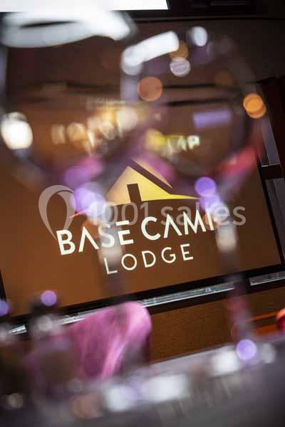 Logo ’Base Camp Lodge’ projeté sur un écran, partiellement visible à travers des verres floutés au premier plan.