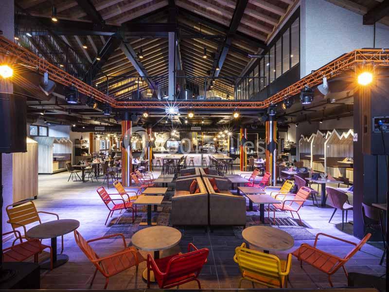 Intérieur d'un espace de restauration moderne avec tables, chaises colorées et éclairage chaleureux sous un toit en bois.