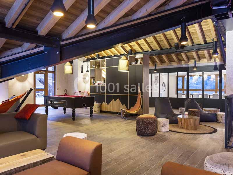 Espace de détente avec billard, fauteuils, poufs et plafond en bois apparent dans un intérieur chaleureux.