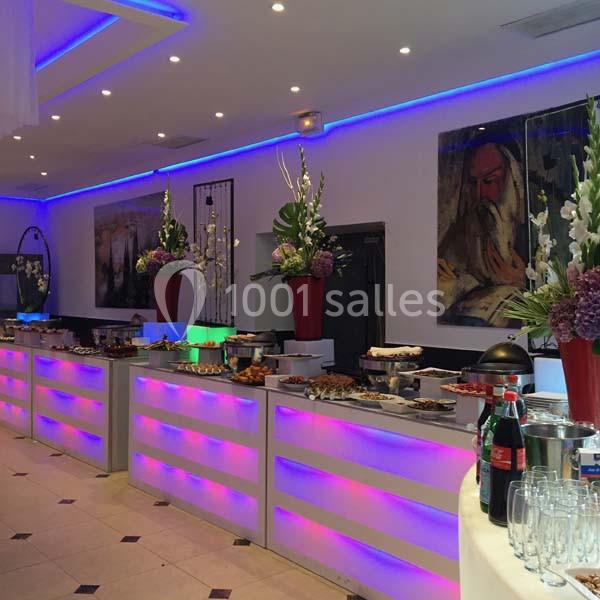 Buffet lumineux avec plats variés, décoré de fleurs et éclairé par des lumières colorées dans une salle moderne.