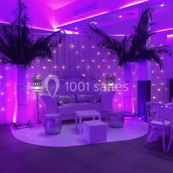 Salon décoré avec des lumières violettes, des palmiers artificiels, un canapé argenté et des lanternes orientales.