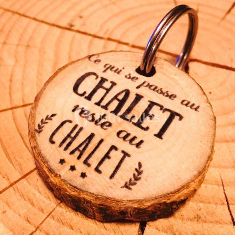 Porte-clés en bois rond avec l'inscription ’Ce qui se passe au chalet reste au chalet’, posé sur une surface en bois.
