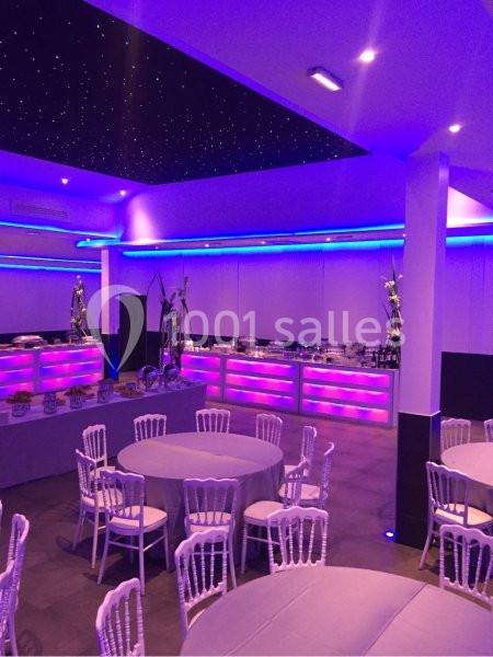 Salle de réception avec tables rondes, chaises blanches et éclairage violet, plafond étoilé en arrière-plan.