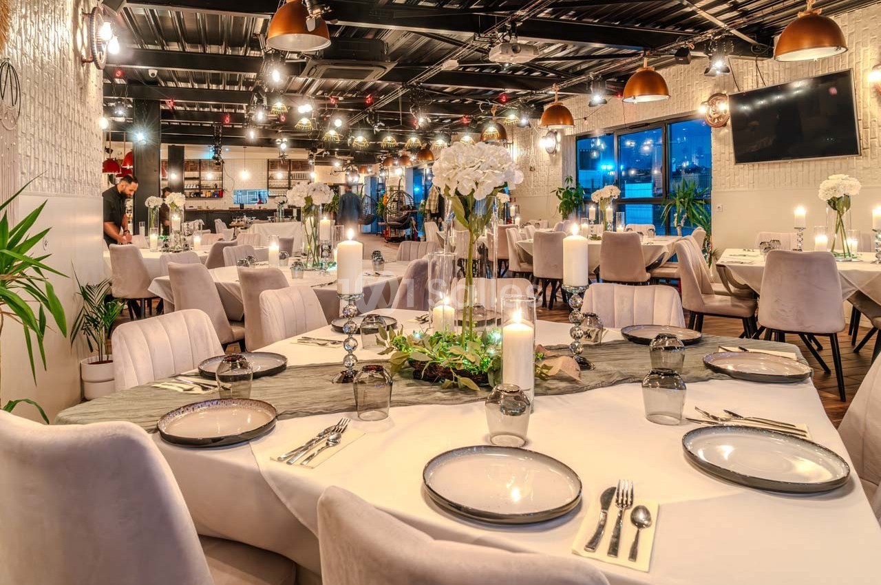 Salle de restaurant élégante avec tables dressées, chandeliers, fleurs blanches et éclairage chaleureux.
