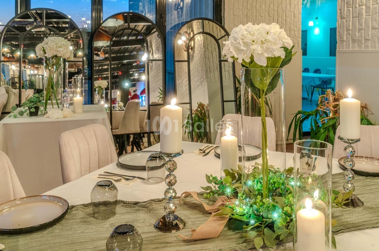 Table élégamment dressée avec bougies, fleurs blanches et décoration végétale dans un cadre lumineux et raffiné.