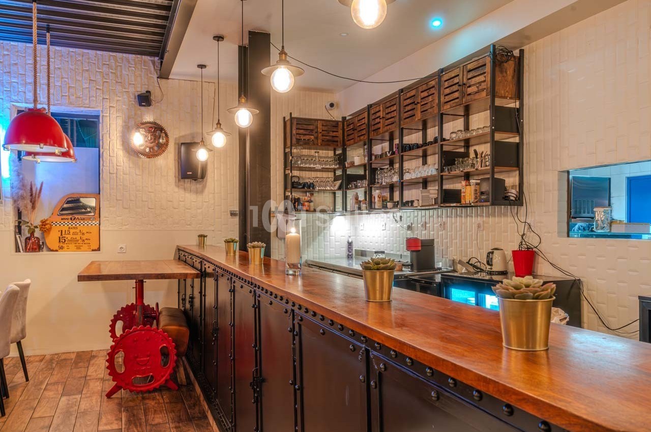 Intérieur d'un café avec un comptoir en bois, étagères murales, suspensions lumineuses et décor industriel.